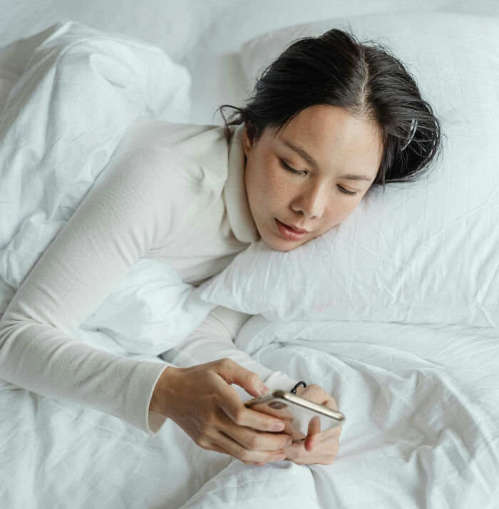 Woman lying in bed, checking her phone with a focused expression, illustrating gut feeling and survival instinct.