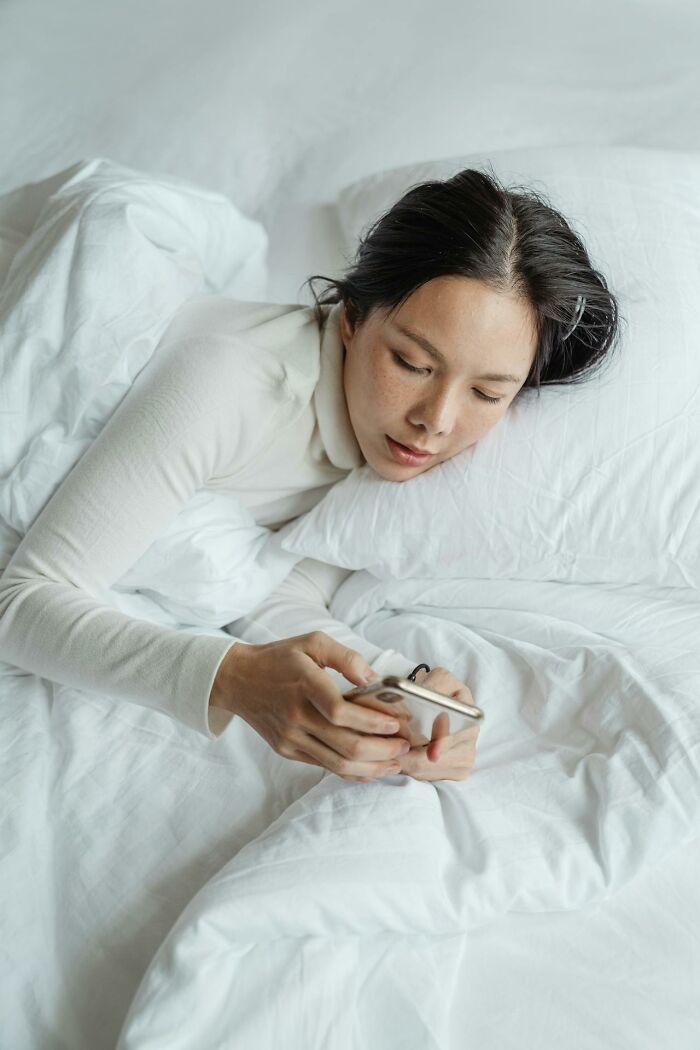 Young woman in white lying in bed using smartphone, reflecting on toxic best friends in a quiet, personal moment. - 16