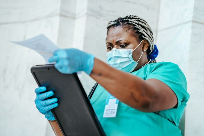 Medical professional wearing mask and gloves examining documents and tablet, dealing with dead bodies and strange details.