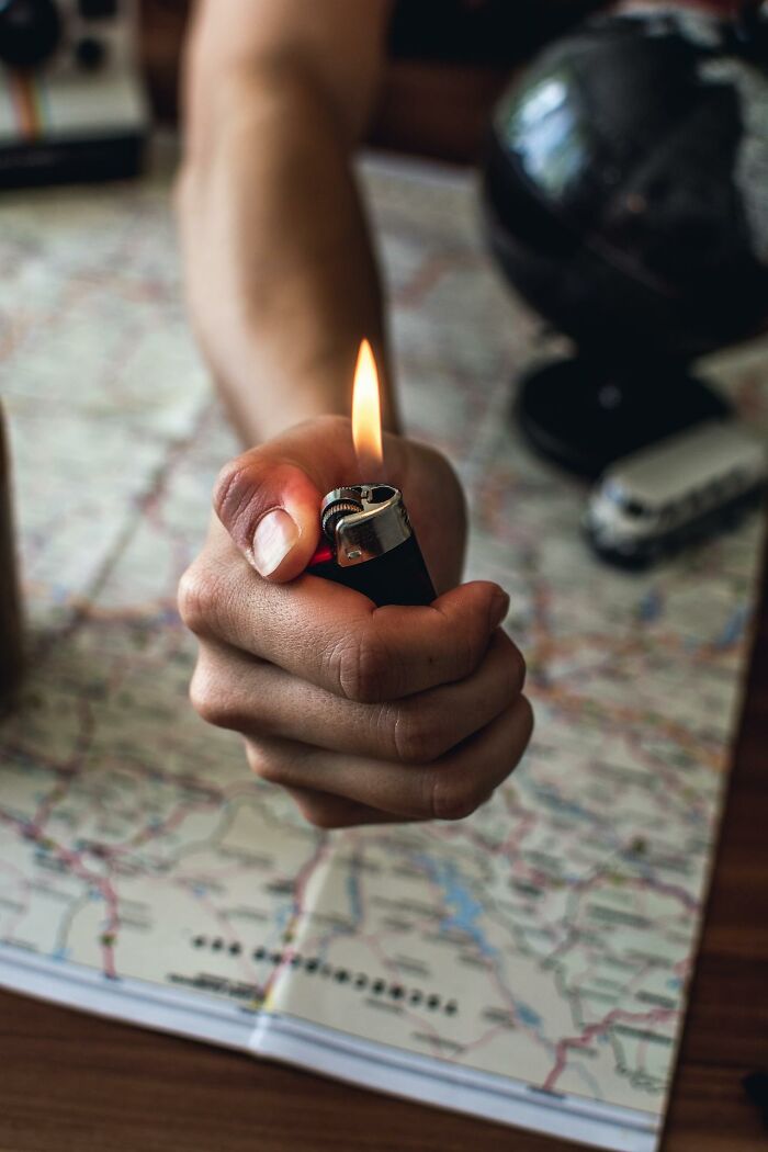 Hand holding a lit lighter over a map, suggesting survival tips in a challenging outdoor or emergency situation.