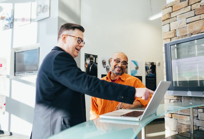 Two men discussing job opportunities on a laptop in a modern office, focusing on six-figure salary careers.