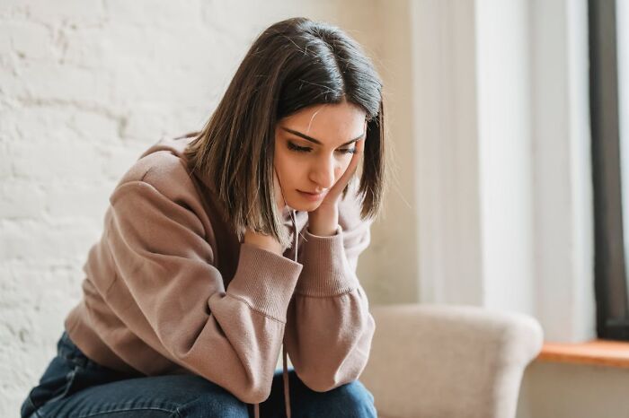 Young woman sitting indoors, looking upset and thoughtful, reflecting on toxic best friends in a quiet room. - 27