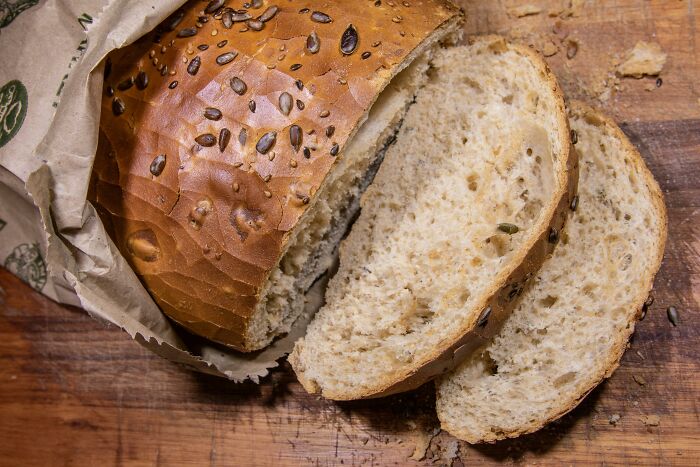 Loaf of multigrain bread partially wrapped in paper with two slices on a wooden cutting board, representing interesting mysteries.