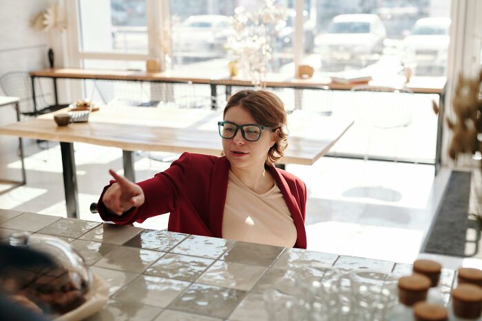 Woman in glasses and red blazer pointing inside a bright restaurant, illustrating McDonald's employees' bizarre experiences.