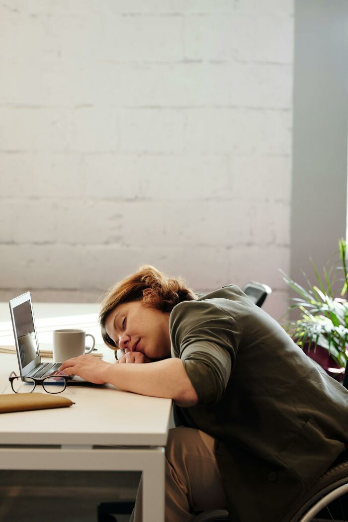 Person exhausted at desk leaning on laptop with coffee cup nearby, symbolizing revenge on bosses through workplace frustration. - 29