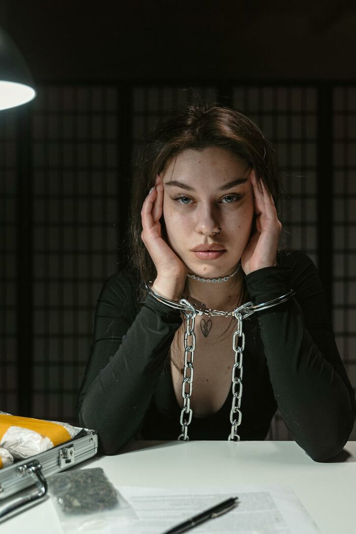 Young woman in chains with stressed expression symbolizing toxic friendship and emotional captivity indoors at a table. - 46