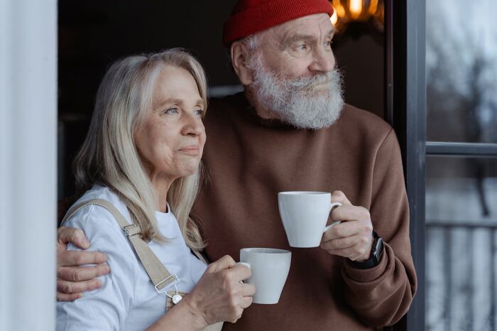 Older couple holding coffee cups, looking thoughtfully outside, illustrating life of older people after divorce. - 18