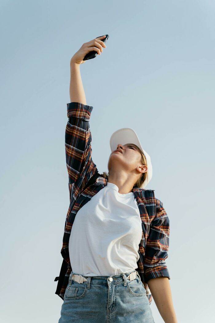 Young woman in casual clothes holding phone up high, symbolizing survival tips and signal searching outdoors.