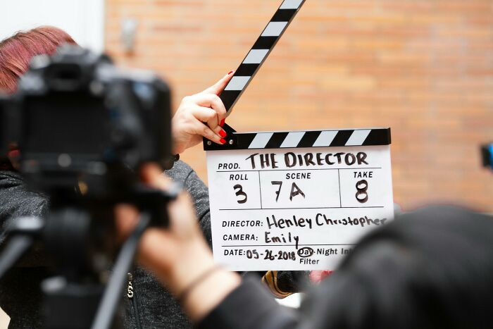 Filming scene with a clapperboard held by a crew member, capturing a moment for movie buffs to identify characters.