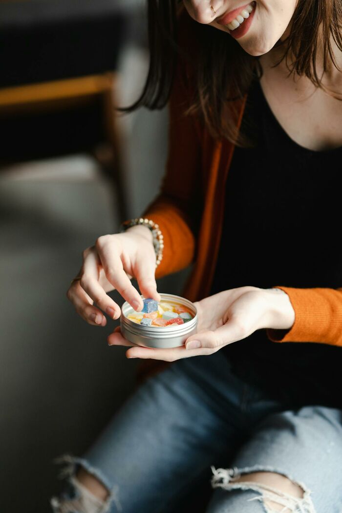 Woman smiling and holding a tin container with colorful gummies, illustrating cheating red flags concept. - 13