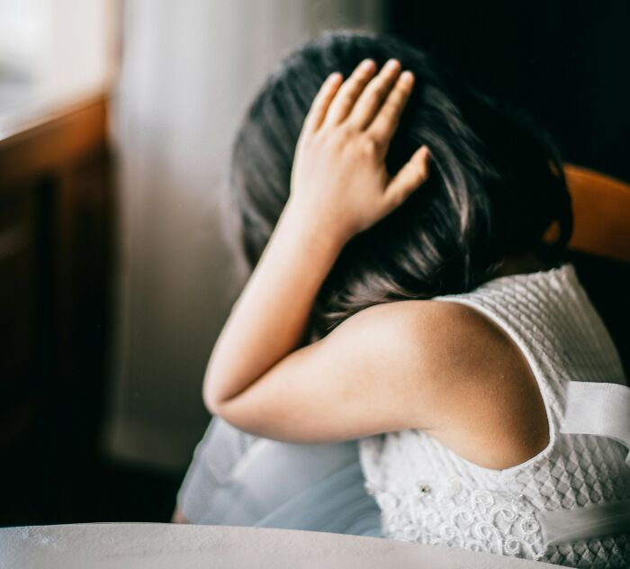 Child sitting with head in hands, reflecting on harmless lies parents told that caused low key trauma. - 15