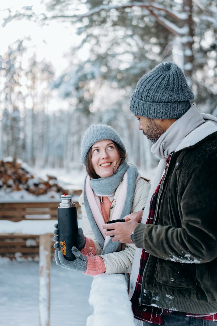 Two people dressed in winter gear sharing a hot drink outdoors, illustrating survival tips in cold weather conditions.