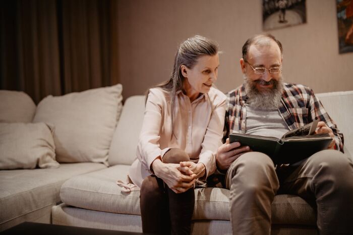 Older couple sitting on a couch, looking through a photo album, reflecting on life after divorce and growing older together. - 24