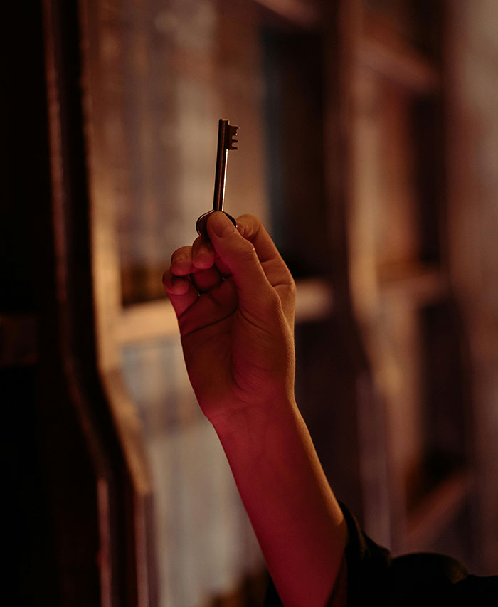 Hand holding an old-fashioned key indoors symbolizing neighbor tales that might make you want to move to the woods.