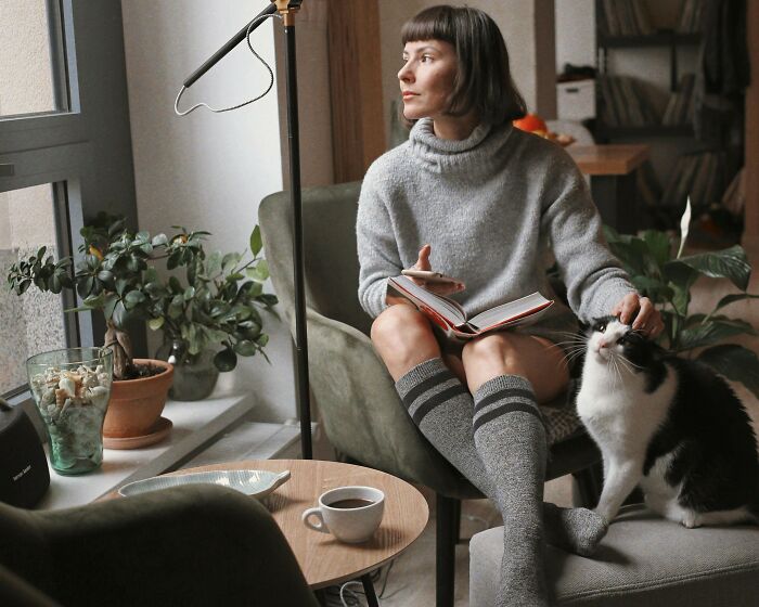 Woman sitting with cat indoors, reading a book and petting the cat during a cat-sitting situation at home. - 3