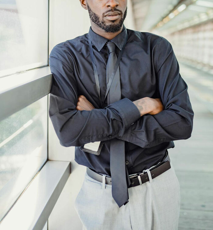 Man in black shirt and tie standing with arms crossed, reflecting on stories of revenge on their bosses. - 13