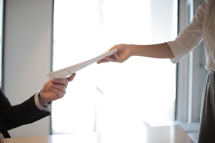 Person handing documents to a boss in an office setting, illustrating stories of revenge on their bosses. - 5