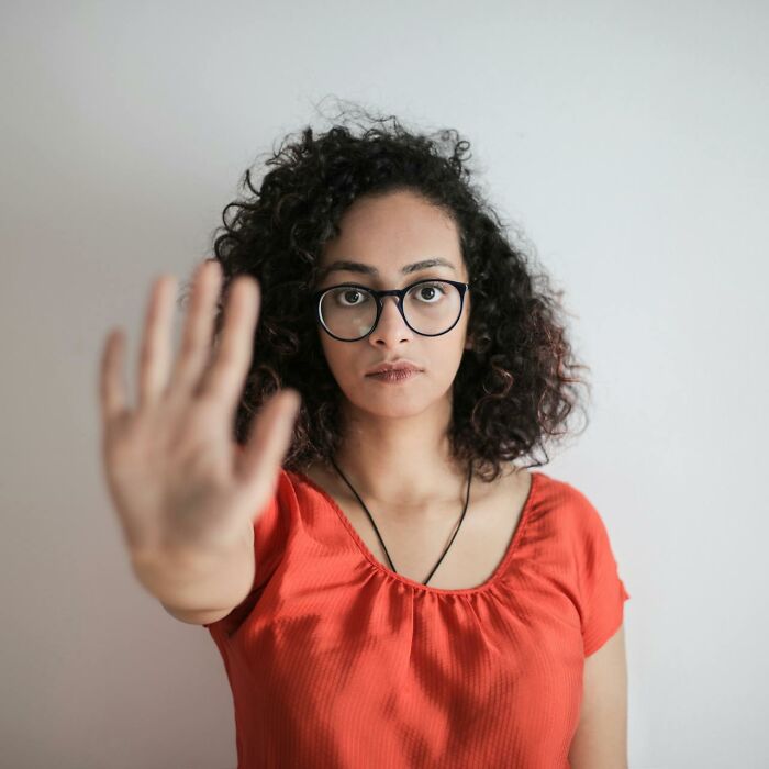 Young woman with curly hair and glasses wearing an orange shirt, holding hand up to emphasize stay hydrated message.