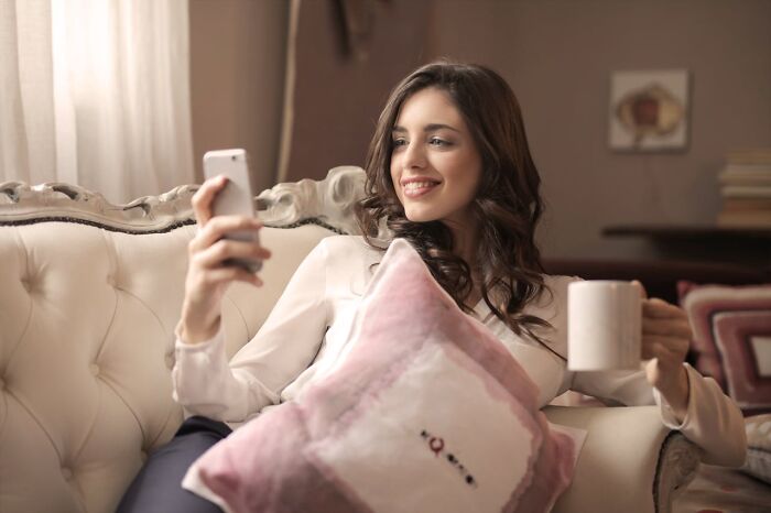 Young woman smiling on couch holding phone and mug, illustrating common cheating red flags in relationships. - 35