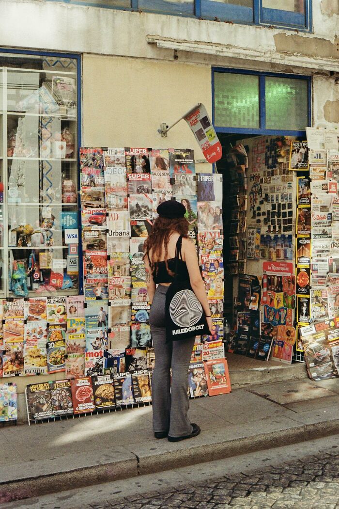 Person with a black beret and tote bag outside a newsstand covered with magazines about revenge on bosses. - 7