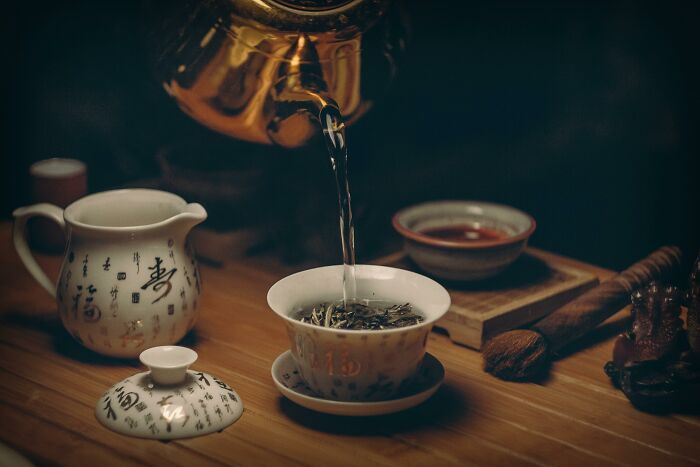 Traditional tea ceremony setup with porcelain cups and a brass kettle pouring hot water on a wooden table, historical events.