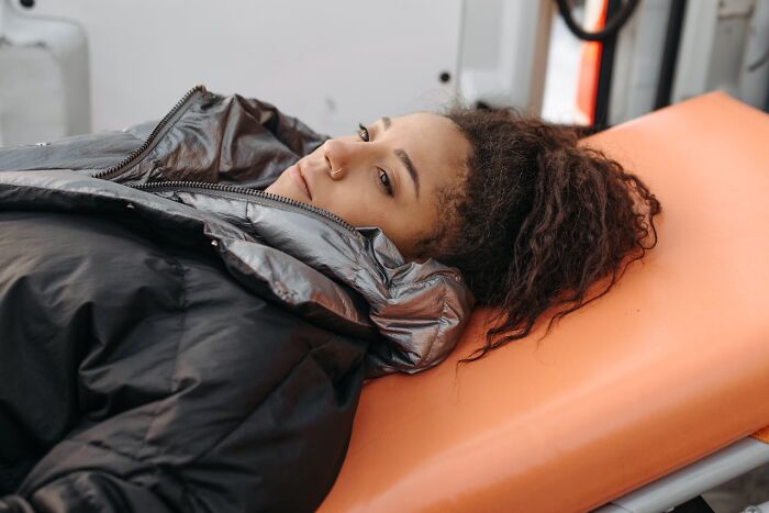 Young woman lying on stretcher inside ambulance, appearing tired and demanding special treatment as an entitled patient.