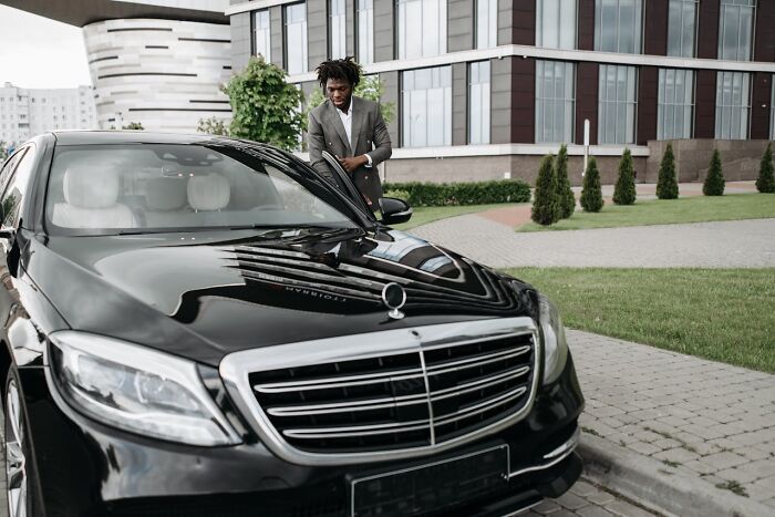 Man in a suit standing next to a luxury car outside a modern office building reflecting revenge on their bosses concept. - 32