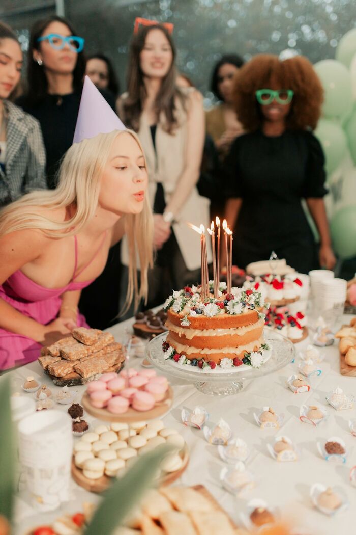 Young woman celebrating birthday with a cake while friends gather, reflecting toxic friendship dynamics in social settings. - 18