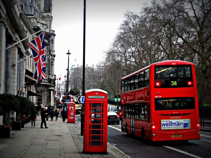 Red double-decker bus and classic red telephone boxes on a London street, representing UK citizenship test facts.