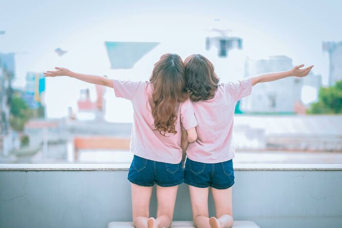 Two girls in matching outfits facing away with arms spread wide, symbolizing the mysteries that still baffle people.