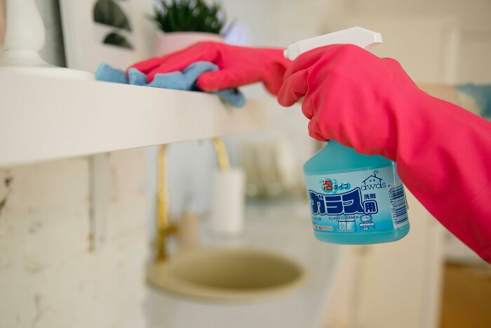 Person wearing pink gloves cleaning a shelf with spray bottle and cloth, symbolizing harmless lies parents told children. - 7