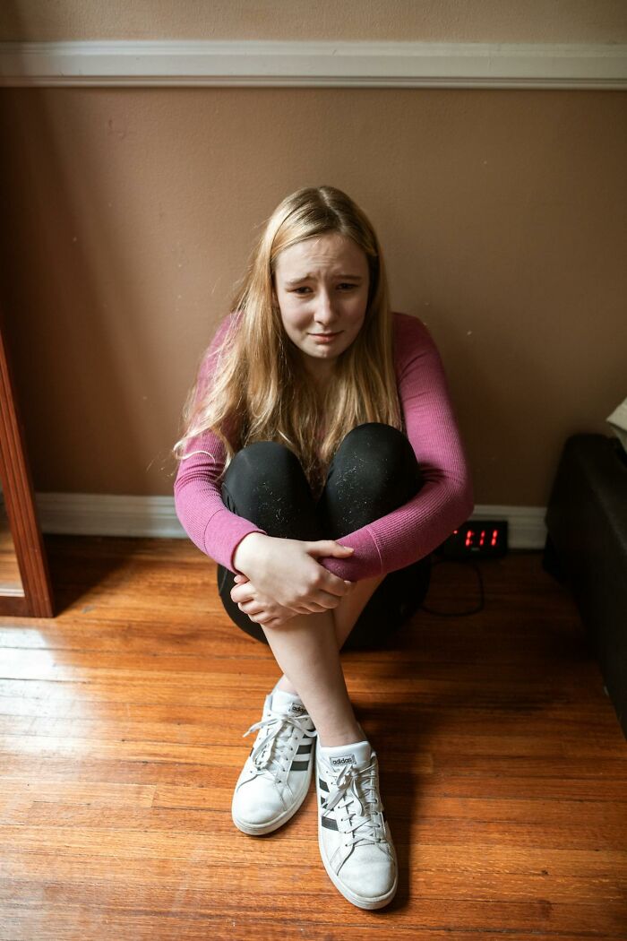 Teen girl sitting on the floor hugging knees, looking upset and reflecting on toxic best friend experiences. - 40