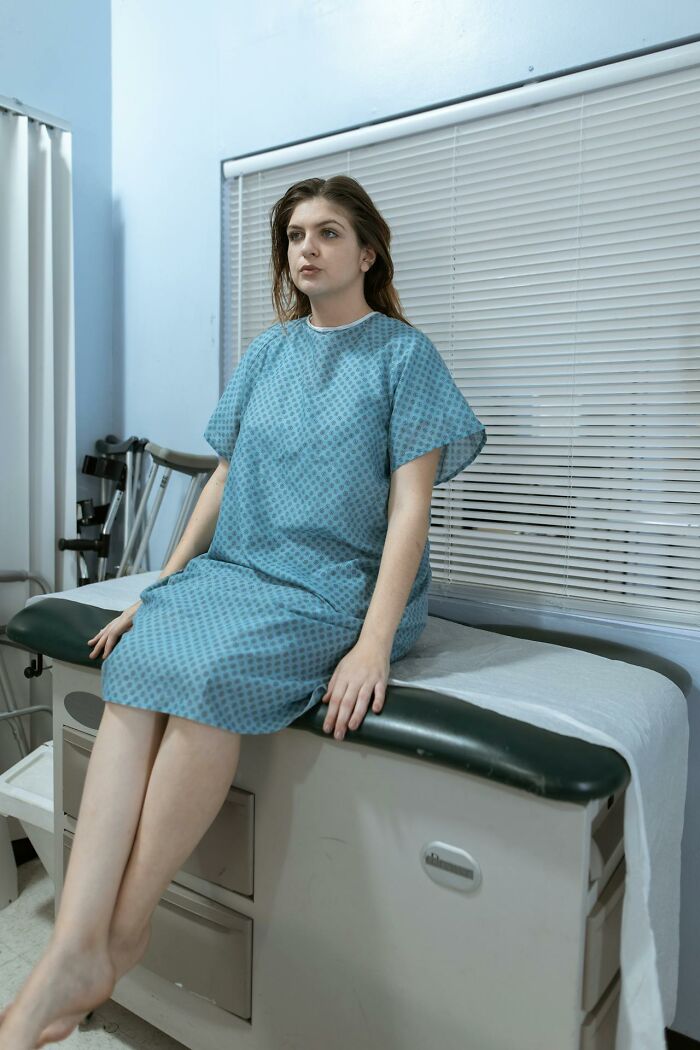 Young woman in a hospital gown sitting on an exam table in a clinical room, illustrating stay hydrated and health care concepts.