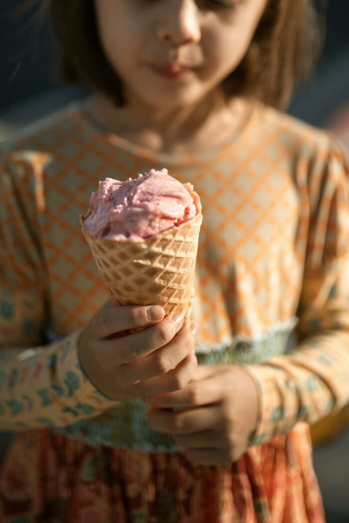 Young girl holding an ice cream cone outdoors, evoking peaceful neighbor tales in a quiet woods setting.