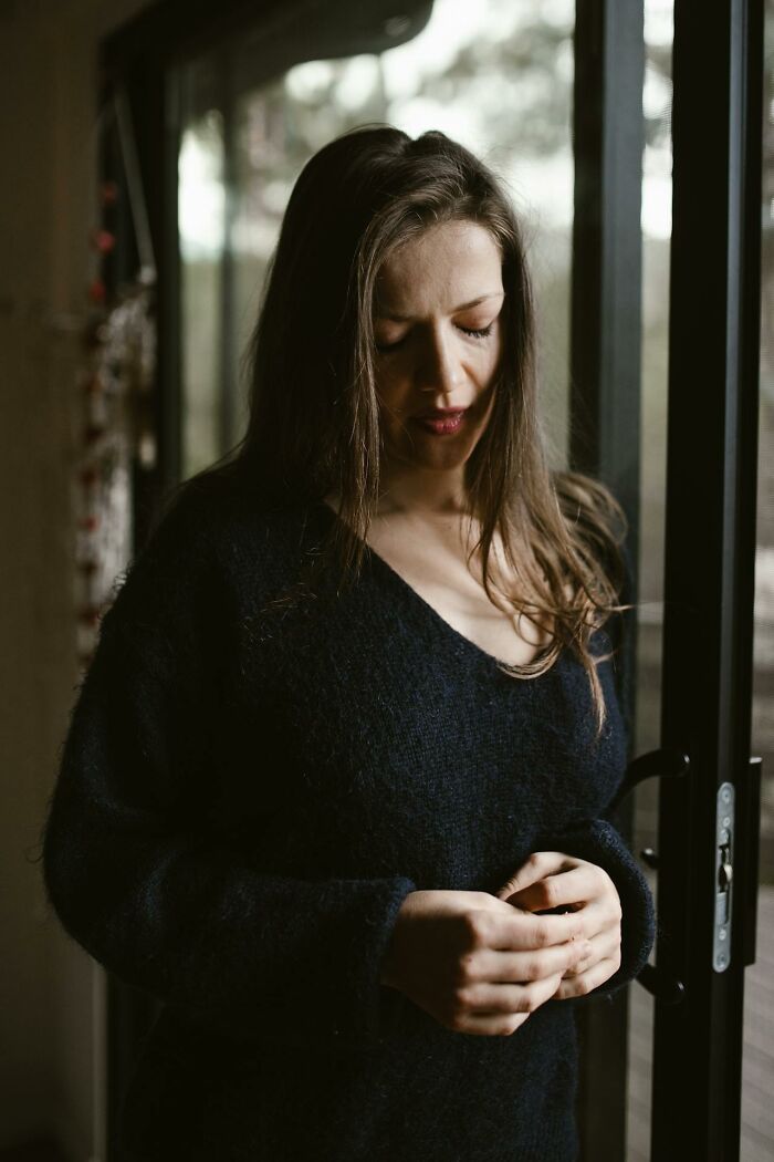 Woman standing by window looking down, appearing thoughtful and reflective about toxic best friends and relationships. - 49
