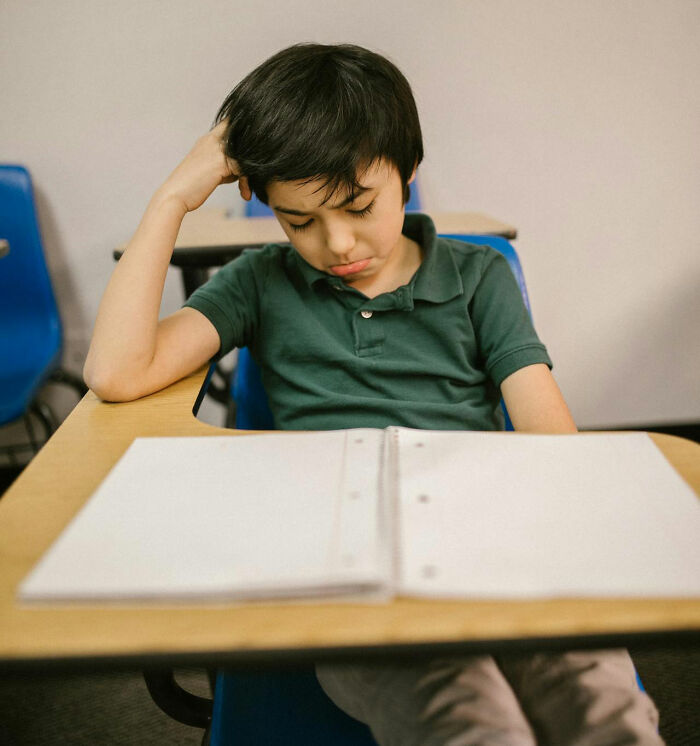 A young boy sitting at a school desk looking upset and distracted, symbolizing disturbing things overheard.