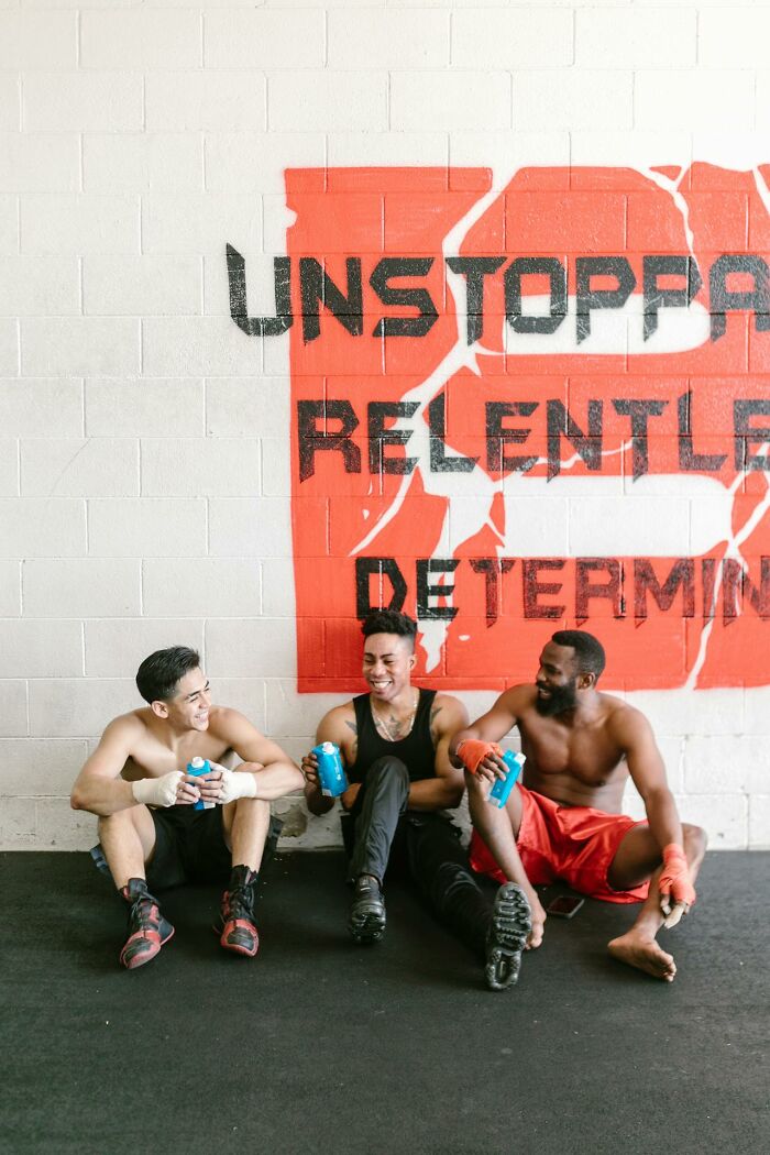 Three men in sportswear sitting against a wall with motivational graffiti, symbolizing determination and relentlessness.