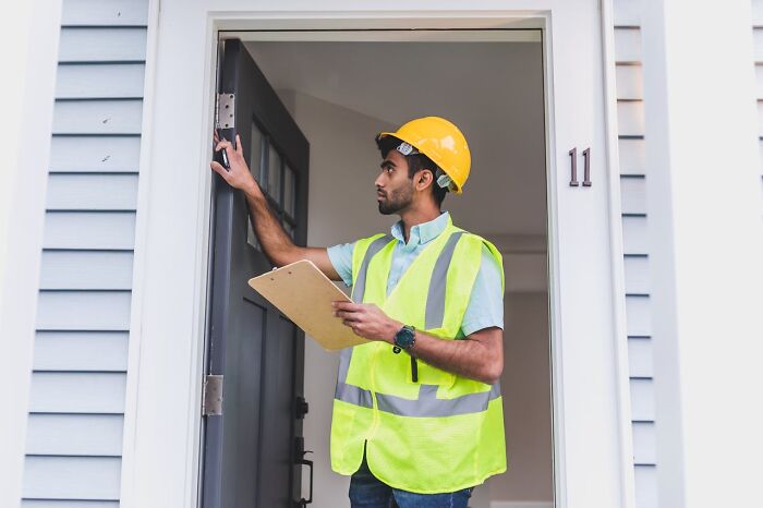 Construction worker wearing a hard hat and safety vest inspecting a door, representing well-paying jobs to make 6 figures.