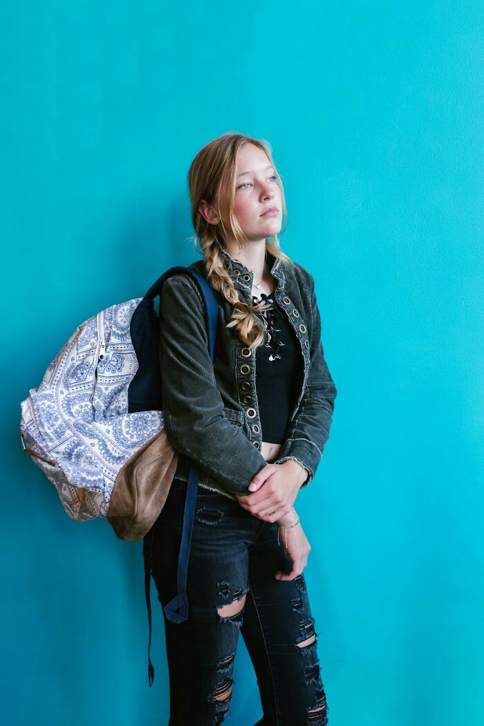 Teen girl with braided hair and backpack standing pensively against a blue wall, capturing disturbing things overheard keywords.