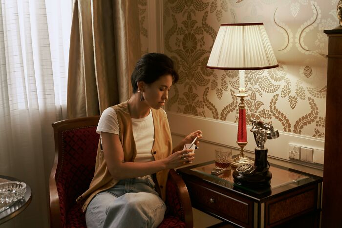Person sitting in a vintage room sharing things that improved life while using a smartphone near a table lamp and drink. - 7