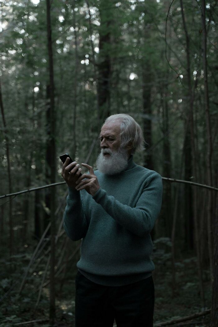 Elderly man in forest wearing teal sweater using smartphone, illustrating survival tips that won't help you at all.