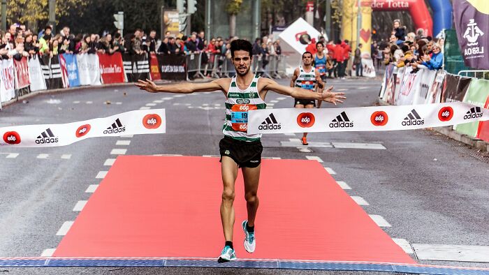 Runner crossing marathon finish line on red carpet with crowd cheering, symbolizing trends leading to overconsumption. - 25