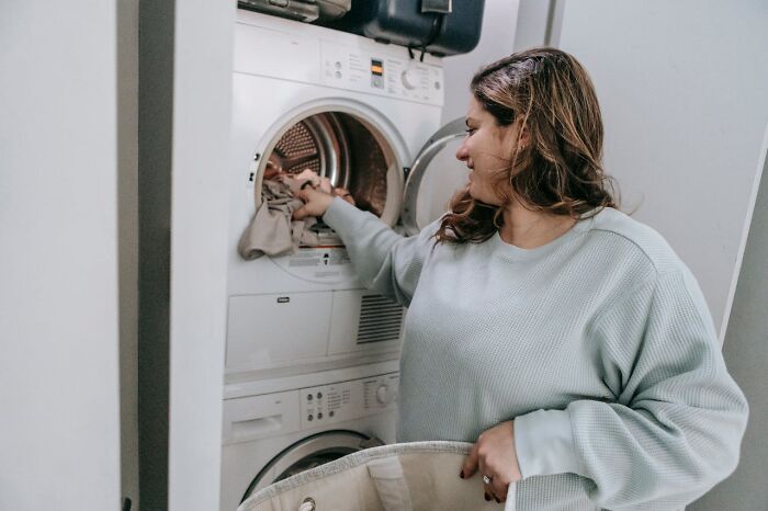 Woman loading laundry into a dryer, multitasking and staying hydrated while managing everyday life tasks efficiently.