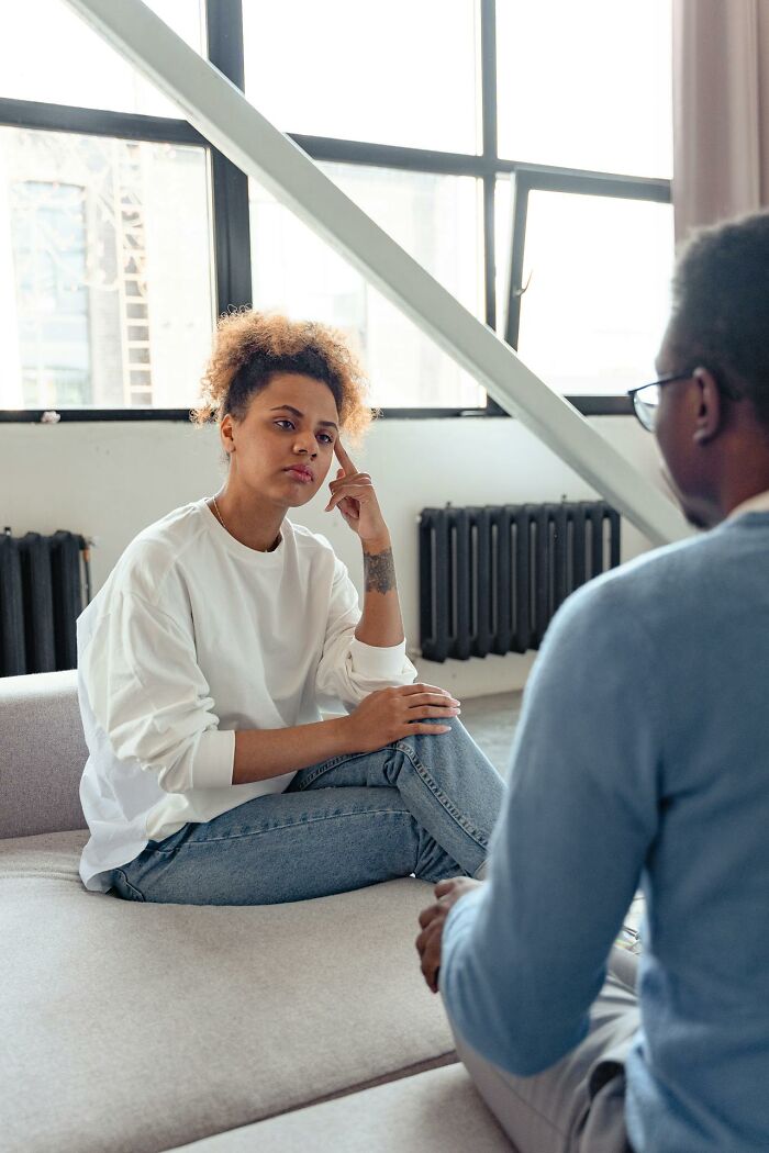 Young woman in casual clothes sitting thoughtfully on sofa, talking to man, emphasizing stay hydrated for wellness.