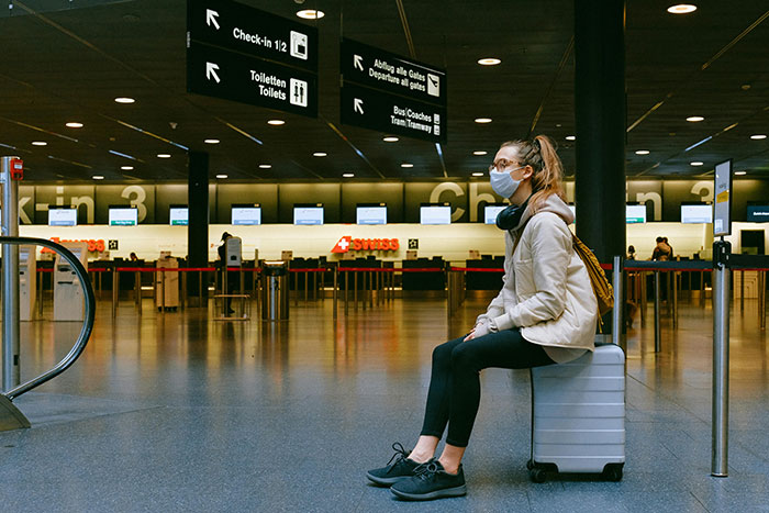 Woman wearing mask sitting on suitcase in airport, trying to survive TSA early morning with noisy child nearby. - 6