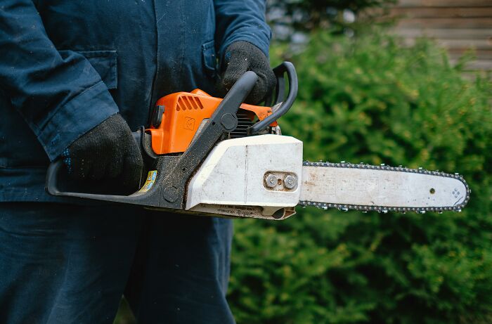 Person wearing gloves holding a chainsaw, illustrating unhinged family lore with a dramatic tool in outdoor setting