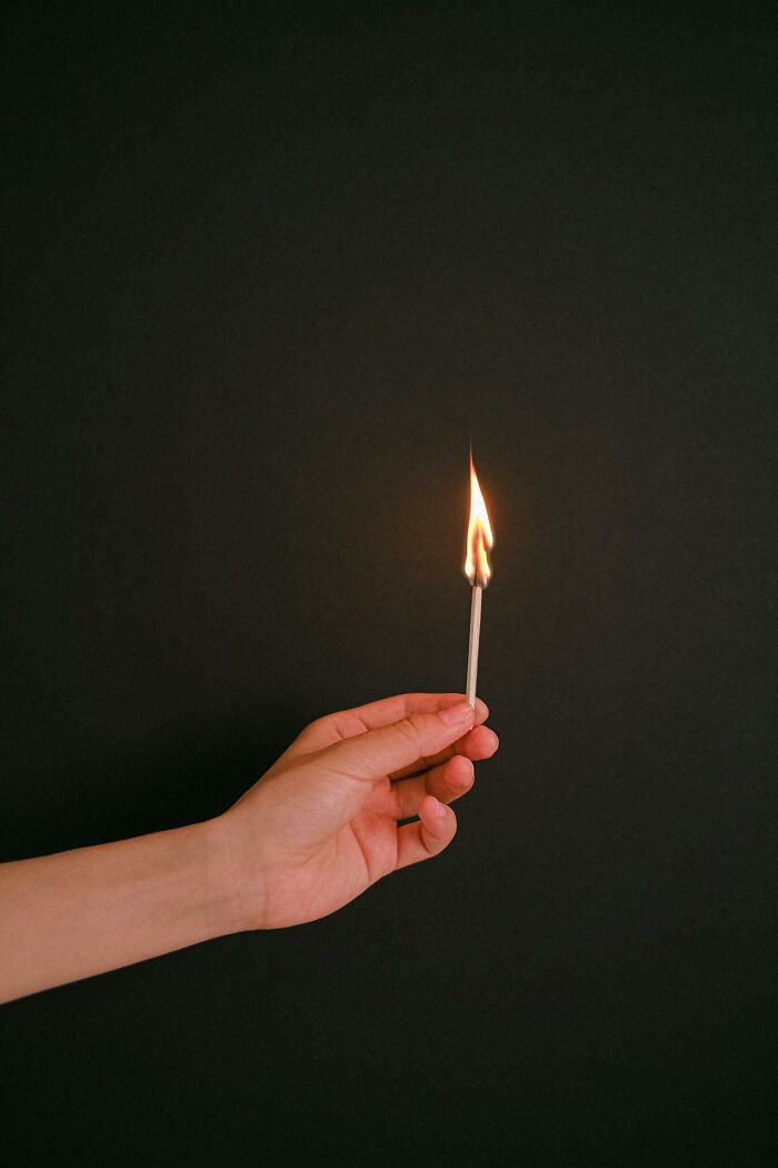 Hand holding a lit matchstick against a dark background illustrating survival tips concept.