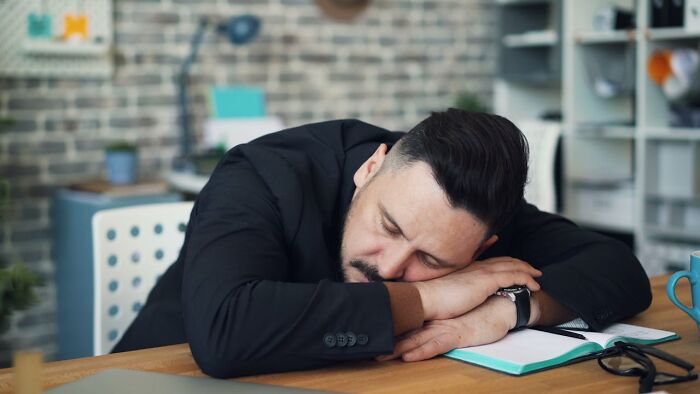 Man in black suit taking revenge on bosses concept, resting head on crossed arms over notebook at office desk. - 36