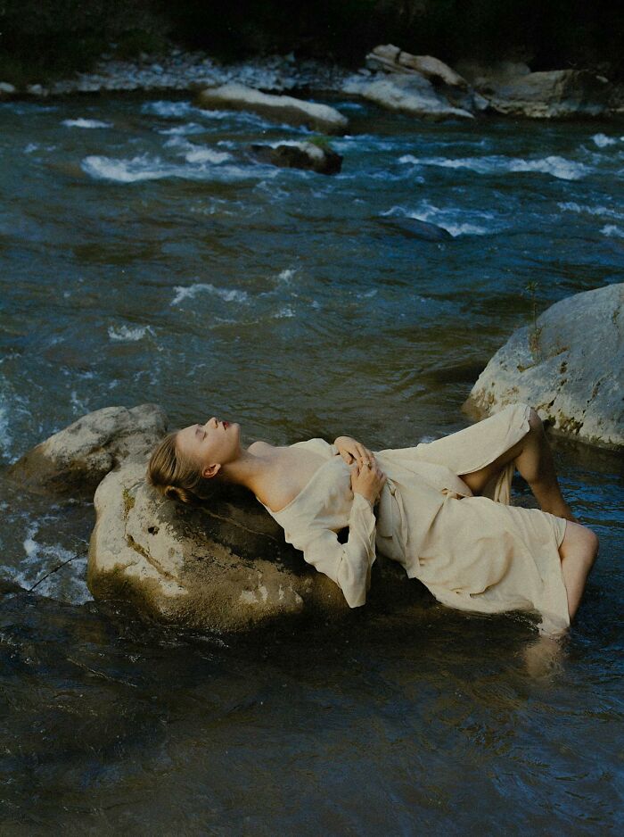 Woman in light dress lying on a rock in flowing river water, illustrating survival tips that won't help you at all.
