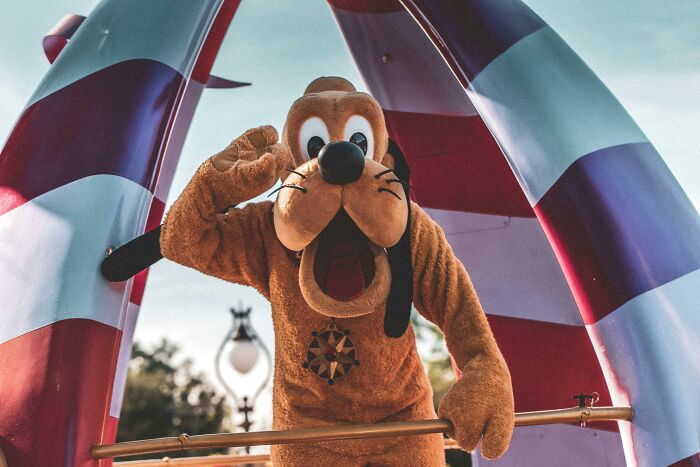 Pluto character posing at a theme park, engaging guests in a Disney quiz about Hakuna Matata meaning.